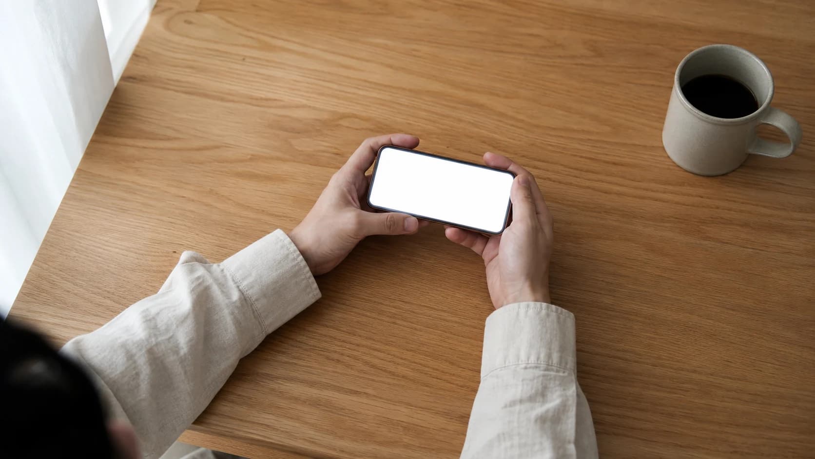 낮의 실내 탁자에서 손에 든 화면을 내려다보는 부감 중거리, 화면 면은 빛으로 날아가 비어 있는 장면