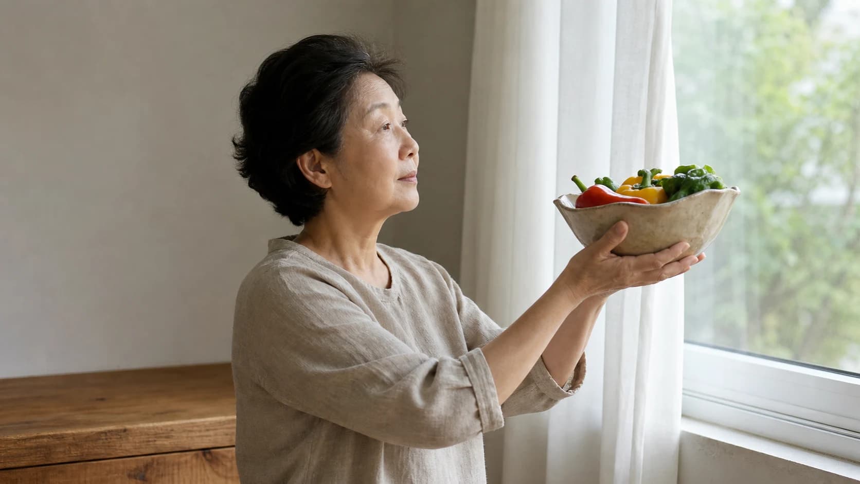 낮의 주방에서 손에 든 것의 색을 확인하려고 창 쪽 밝은 자리로 가져가는 중거리 옆모습