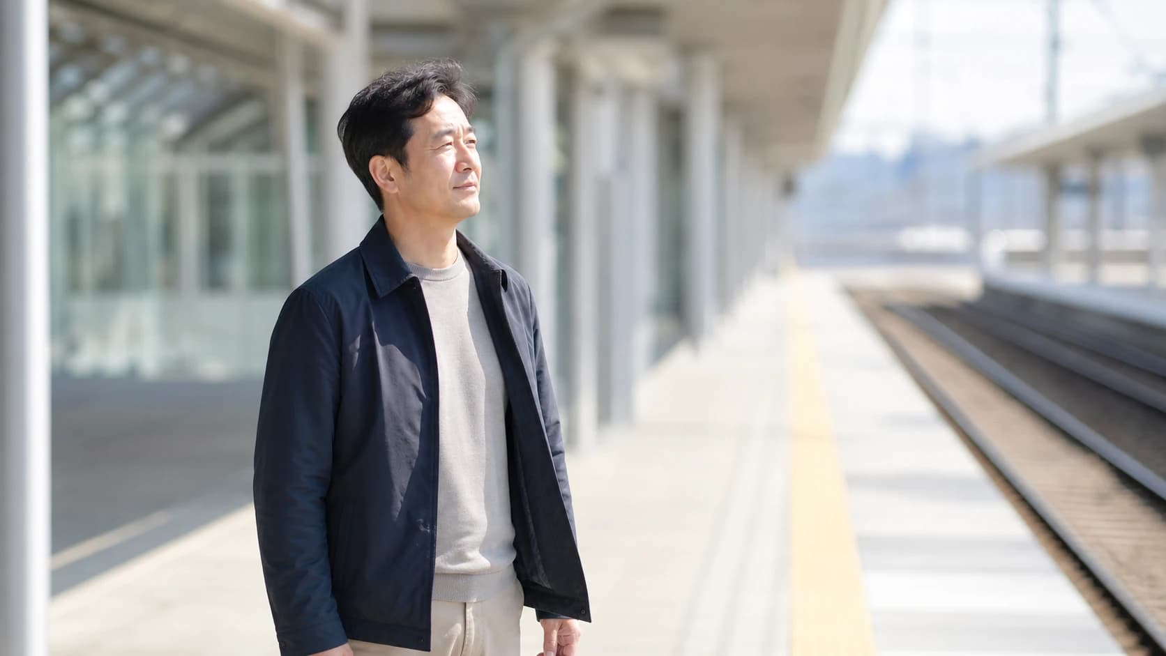 밝은 낮 역 승강장에서 눈을 살짝 찡그린 채 서 있는 사람